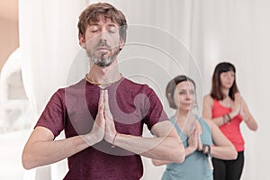 The man in the foreground with the hands in Namaste`s gesture. Close up of man meditating at yoga studio. How to Keep Your Arms i