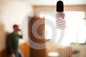 A man, a foreman in a cap, is talking on the phone in a distant room. Against the background of an energy-saving lamp