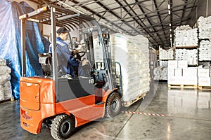 A man on a forklift works in a large warehouse, unloads bags of raw materials