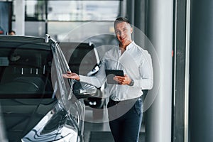 Man in formal clothes is standing indoors near moden new car