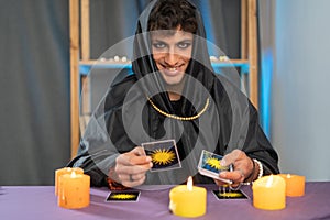 Man fortune teller reading the future by tarot cards sitting at a table with candles