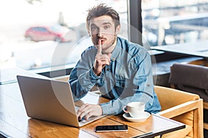 Man freelancer working on laptop, showing shh gesture, looking at camera, asking not to make noise