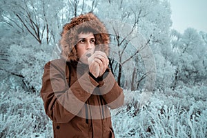 Man freezes in the cold in the forest and tries to wipe his hands with his breath. The concept of frostbite of the extremities