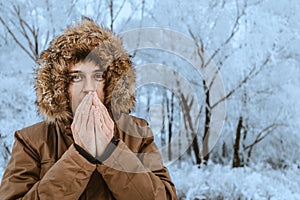 Man freezes in the cold in the forest and tries to wipe his hands with his breath. The concept of frostbite of the extremities
