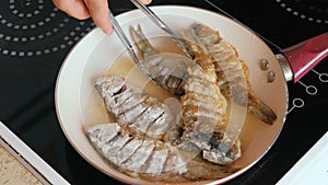 Man fried fish in oil in a pan. Close-up man`s hands flips fish with culinary tongs.