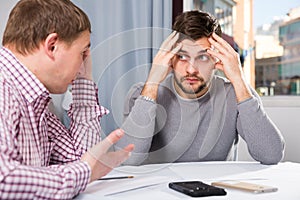 Man with friend looking worriedly at papers at home table