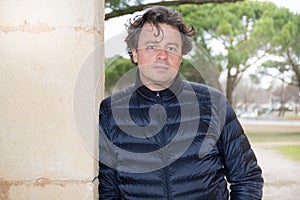 Man with a friendly smile leaning casually against wall with a rough texture outdoors