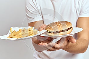 A man with fries and a hamburger on a light background in white t-shirt close-up cropped view Copy Space Model