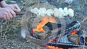a man fries and turns over champignon porcini mushrooms, which are planted on hats over an open fire