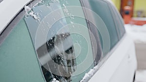 A man frost scratches the side window of his car on a cold winter morning