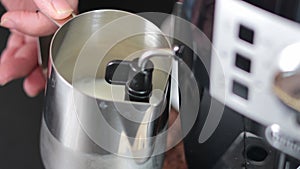 A man froths milk in a metal mug with a cappuccinatore in a coffee maker. Close-up of a mug with milk.