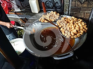 man frying cripsy tofu at big pan, using used cooking oil or minyak jelantah