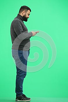 A man, full-length, on a green background, with a phone