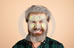 Man with fun facial mask with Cucumber. Spa man applying facial clay mask. Home spa. Men holding pieces of cucumber on