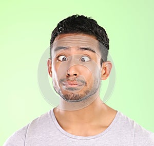 Man, funny face and silly in studio, crosses eyes and goofy comic or humor on green background. Male person, mockup