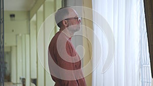 The man in the gallery standing at the window considering artwork.