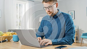 Man in Galsses and Navy Blue Shirt Sitting at the Table at Home and Working on His Modern Silver L