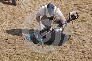 Man gardener cleaning machine scarifier from old dry grass on the lawn