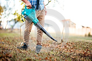 Man Gardener clearing up leaves using an electric leaf blower tool. Gardening details