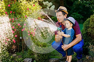 Man gardener with grandson watering garden
