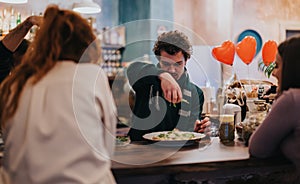 Man Garnishing Dish While Friends Enjoy Atmosphere in Cozy Cafe Setting photo