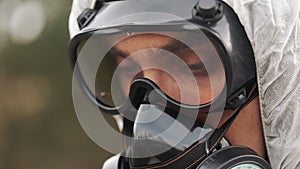 Man in gas-mask and bio-hazard suit looks down taking notes on his tablet