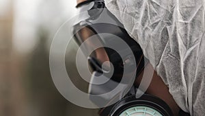 Man in gas-mask and bio-hazard suit looks down taking notes on his tablet