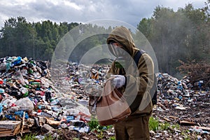 A man in a gas mask examines the contents of the bag. The worker is in the dump. Around burns and smokes plastic garbage