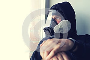 A man in a gas mask looking out the window crossed his hands in the foreground