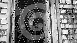 A man with a gas mask looks from window with bars and can not go free