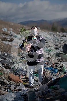 Man with gas mask and plant on landfill, environmental concept.