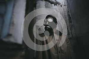 A man in gas mask standing inside an old building, peeking around the corner