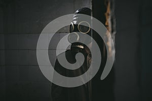 A man in gas mask standing inside an old building, peeking around the corner