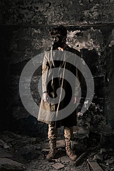 Man in gas mask standing near old wall in abandoned room