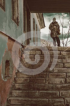 A man in a gas mask stands on the steps of a destroyed house