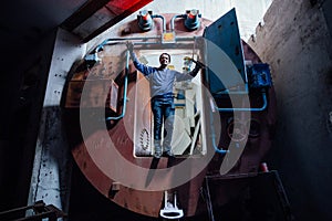 Man in gateway corridor of airlock of abandoned bunker. Big hermetic door illuminated by red lantern