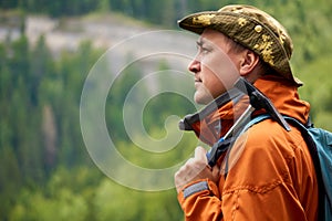 Man geologist with a backpack and a geological hammer in hand against the backdrop of a wooded mountain landscape