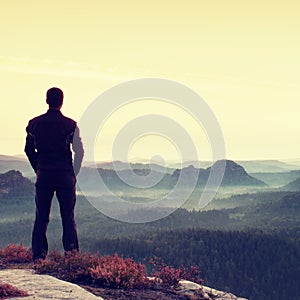 Man gesture triumph. Satisfy hiker in dark sportswear at edge with heather.Tall man on the peak of sandstone cliff watching to lan