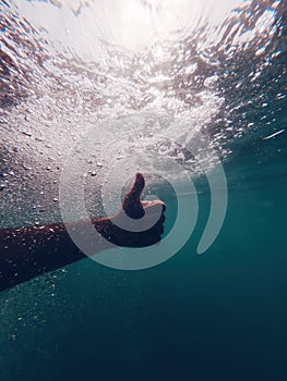 Man gesturing thumbs up underwater in deep sea water as sign of endorsement and approval