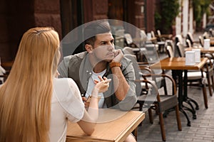 Man getting bored during date with overtalkative young woman at outdoor cafe