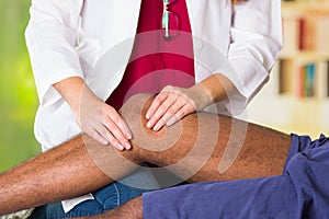 Man getting knee treatment from physio therapist, her hands holding his leg and applying massage, injury medical concept photo