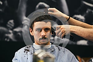 Man getting trendy haircut at barber shop. Male hairstylist serving client, making haircut using machine and comb