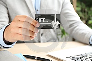 Man with gift card and laptop at table indoors, closeup