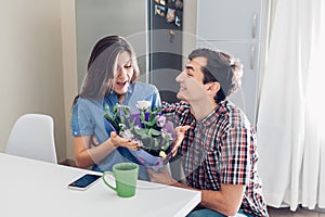 Man gifting bouquet of flowers to his girlfriend on kitchen at home. Valentines day romantic surprise