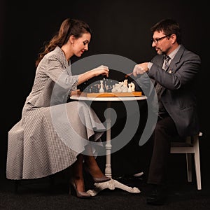A man with a girl plays chess and smokes a pipe on a dark background