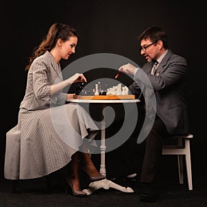 A man with a girl plays chess and smokes a pipe on a dark background