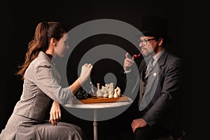 A man with a girl plays chess and smokes a pipe on a dark background