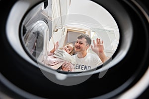Man and girl view from washing machine inside. Father with daughter does laundry daily routine