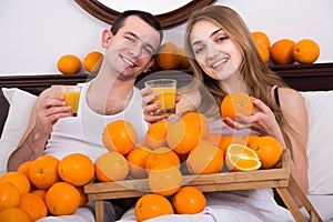 man and girlfriend drinking squeezed orange juice in bed