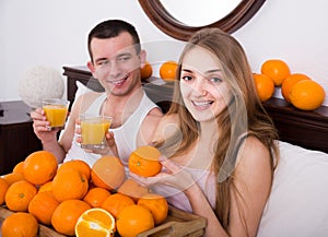 man and girlfriend drinking squeezed orange juice in bed